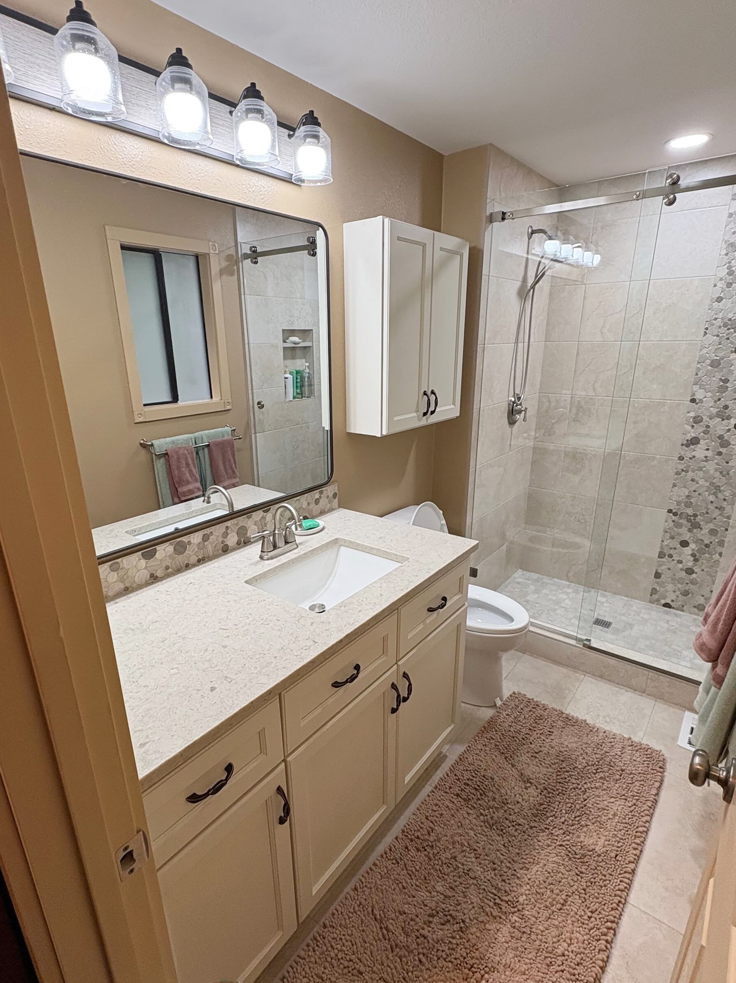 Vanity Detail — Remodeled bathroom with a cream vanity, quartz counter, framed mirror, and glass walk-in shower