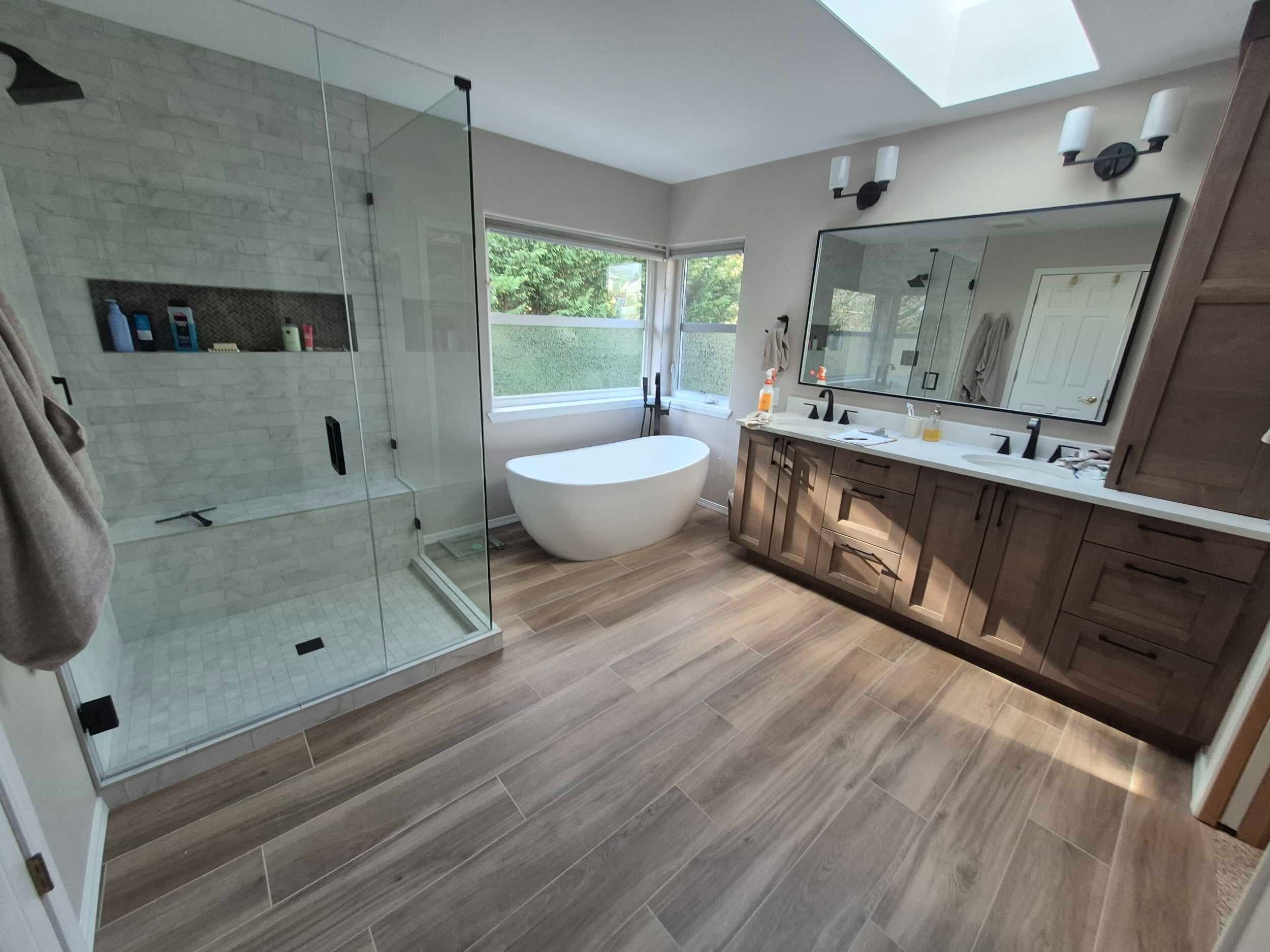 Bathroom Remodeling — Remodeled bathroom with a glass walk-in shower, freestanding tub, double vanity, and skylight