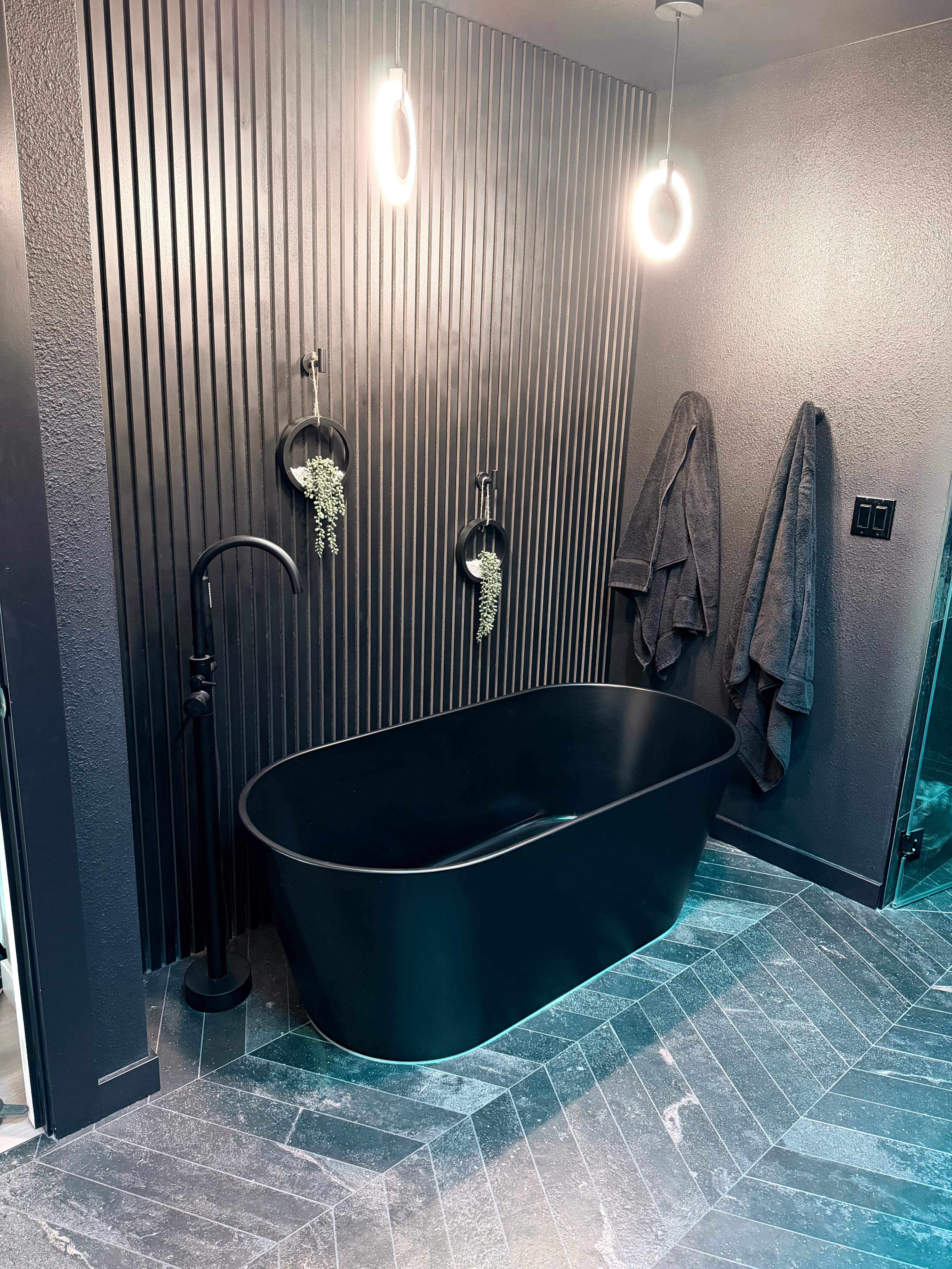 Project Evidence — Dark modern bathroom with a black freestanding tub, slatted accent wall, and chevron tile