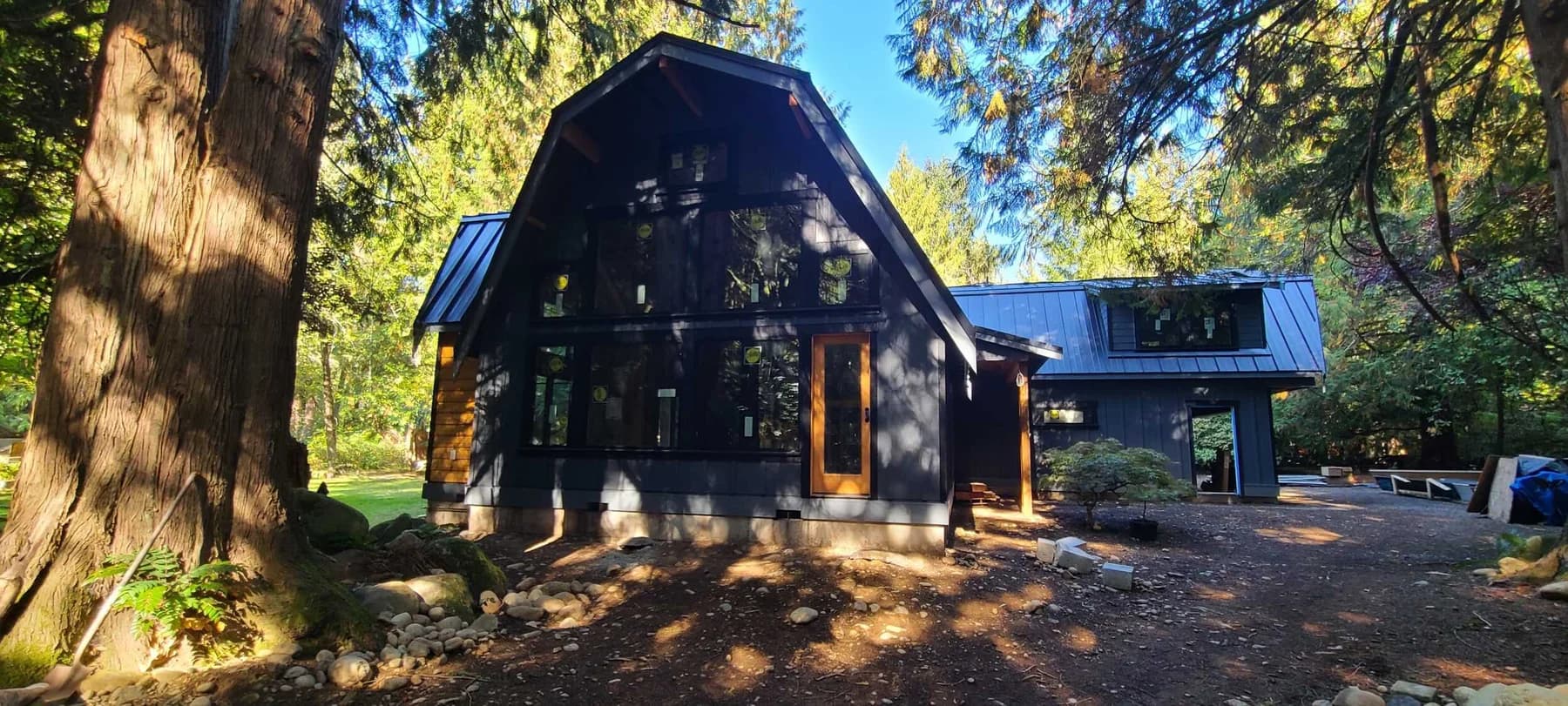 Custom Home Exterior — Custom home with dark siding, a gambrel roof, large windows, and wood entry doors