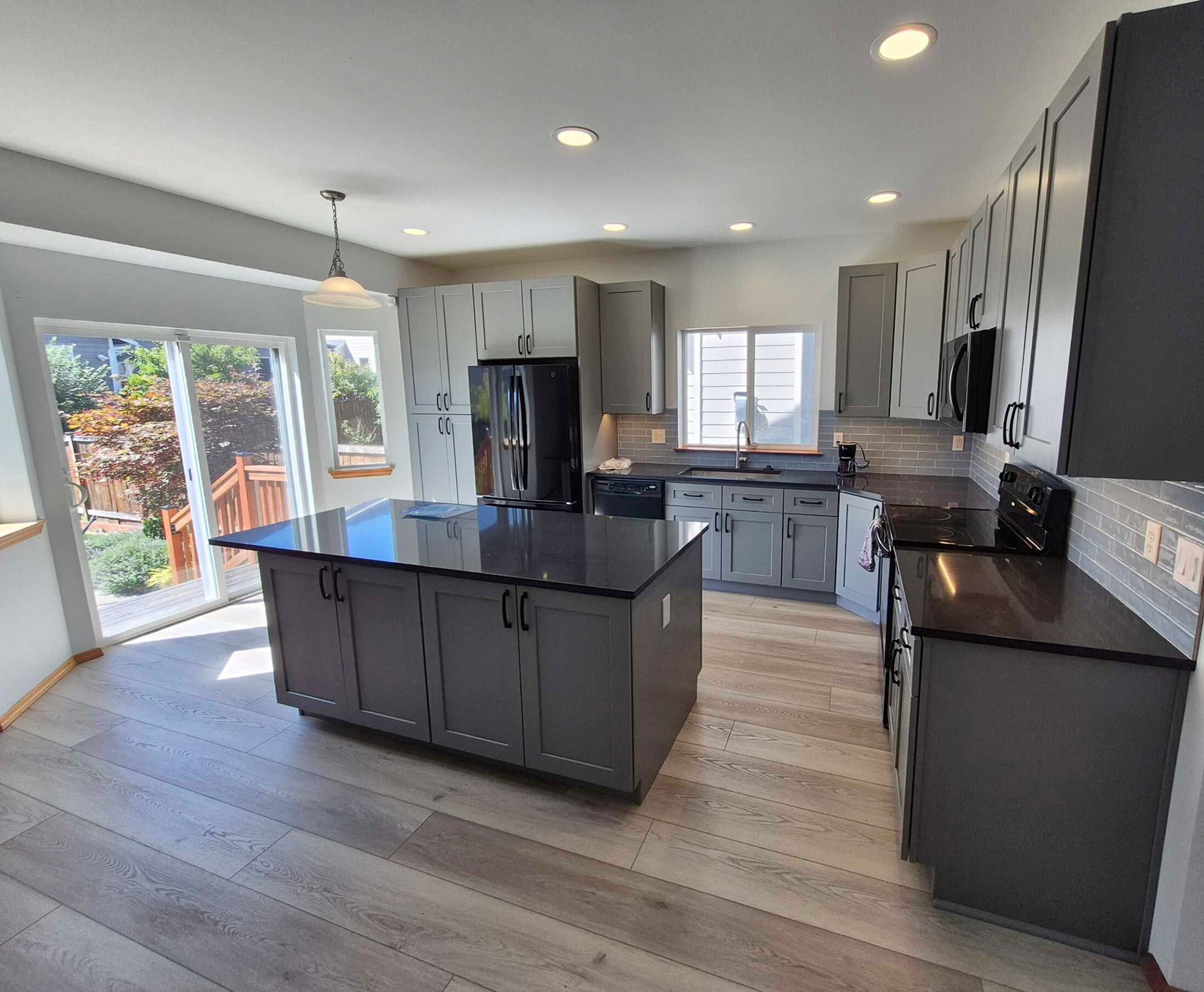 Kitchen Remodeling — Remodeled open kitchen with a large dark-countertop island, gray shaker cabinets, and wide-plank flooring