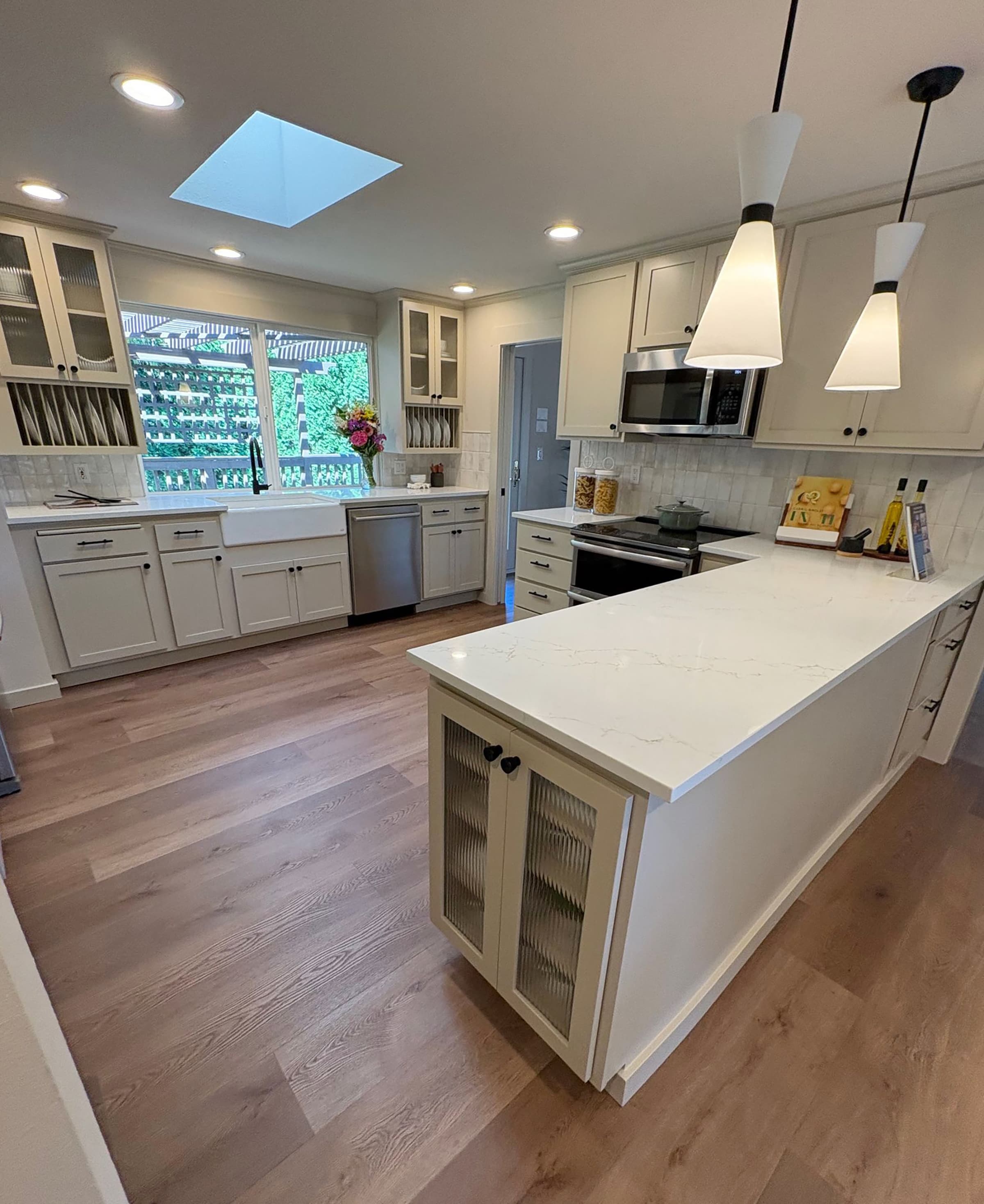 Storage Detail — Bright remodeled kitchen with white cabinetry, quartz peninsula, farmhouse sink, and a skylight