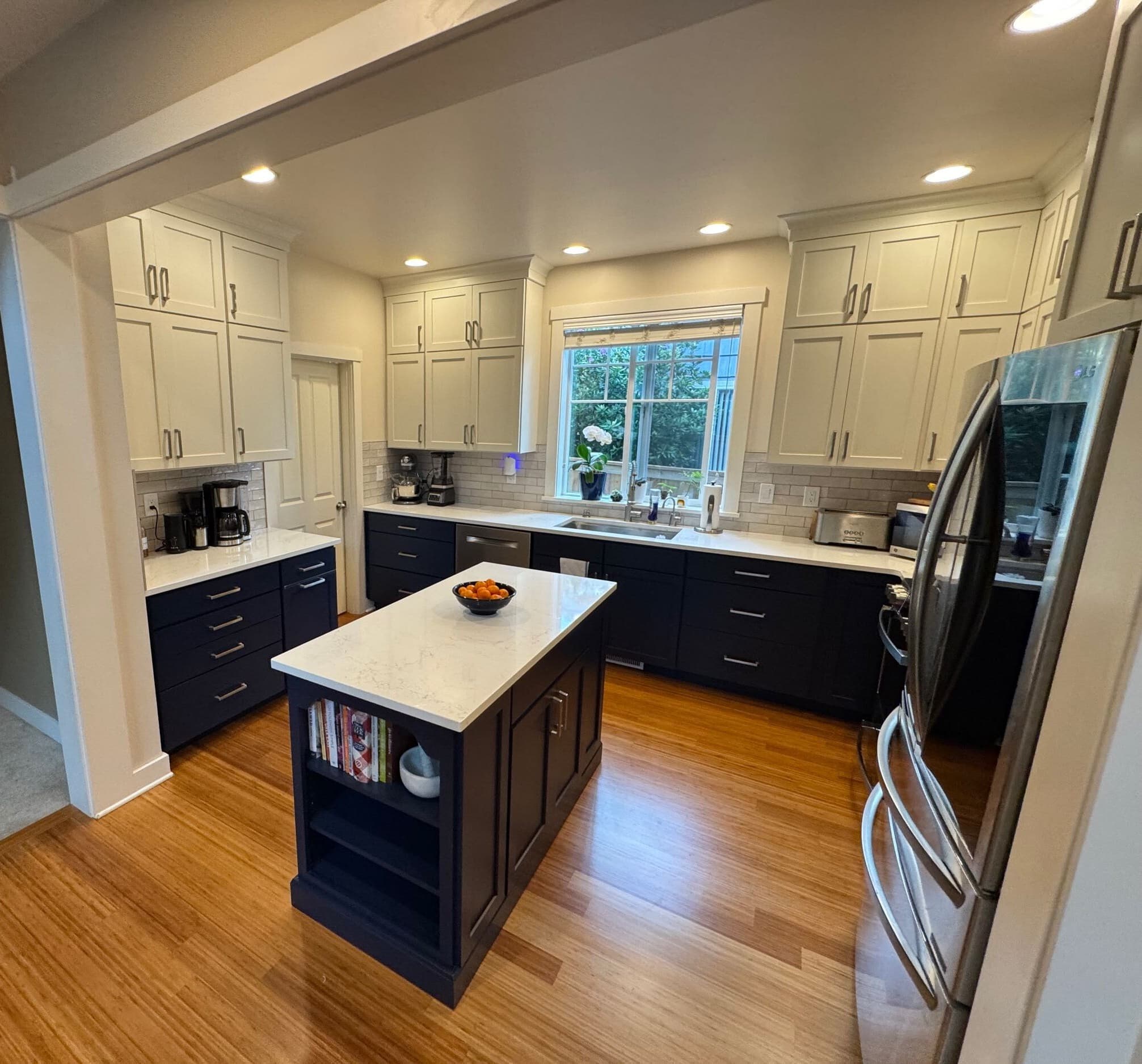 Tubro kitchen remodel with navy and white cabinetry, a central island, and warm wood flooring