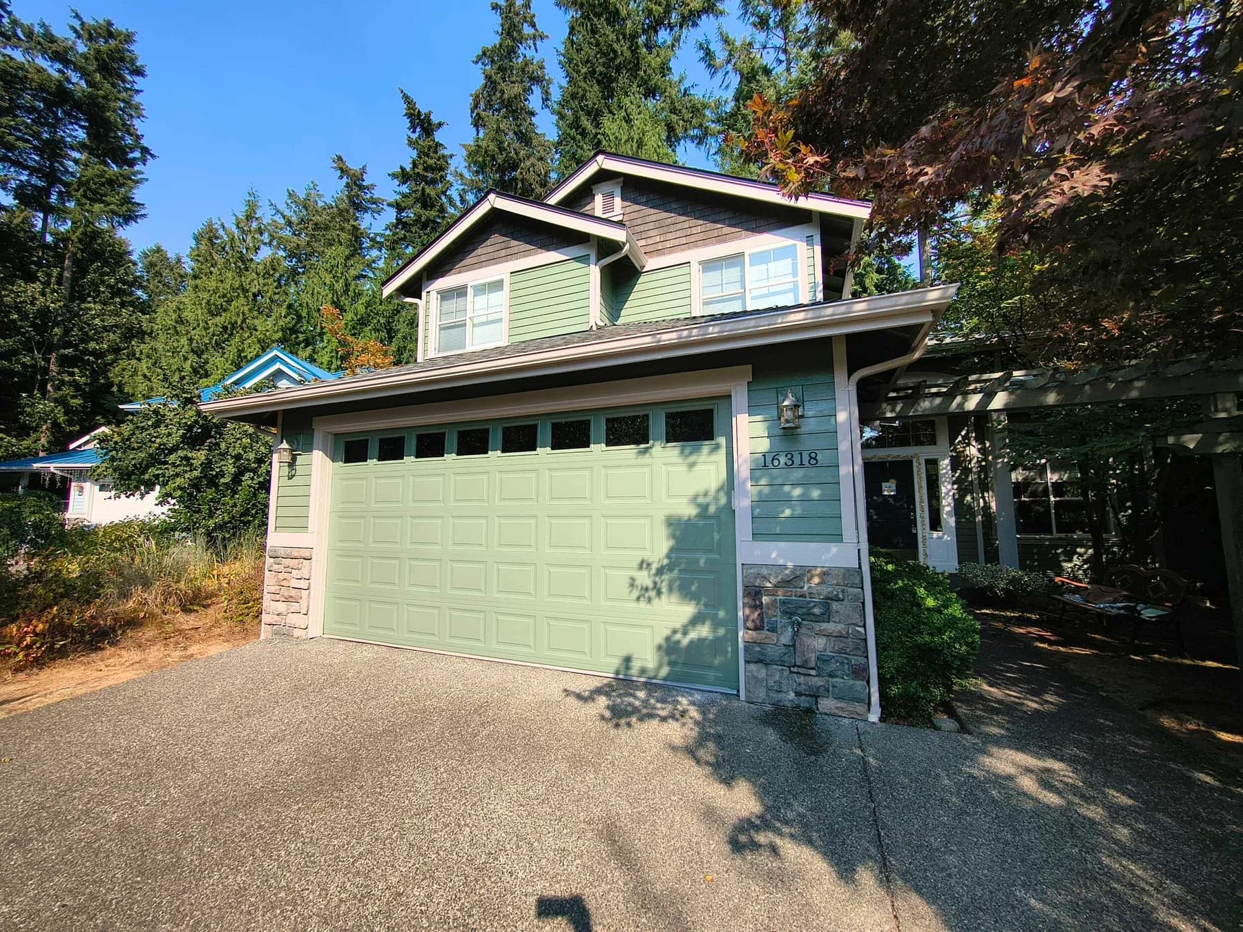 Exterior Painting — Two-story home with green siding and garage door, light trim, and stone accents