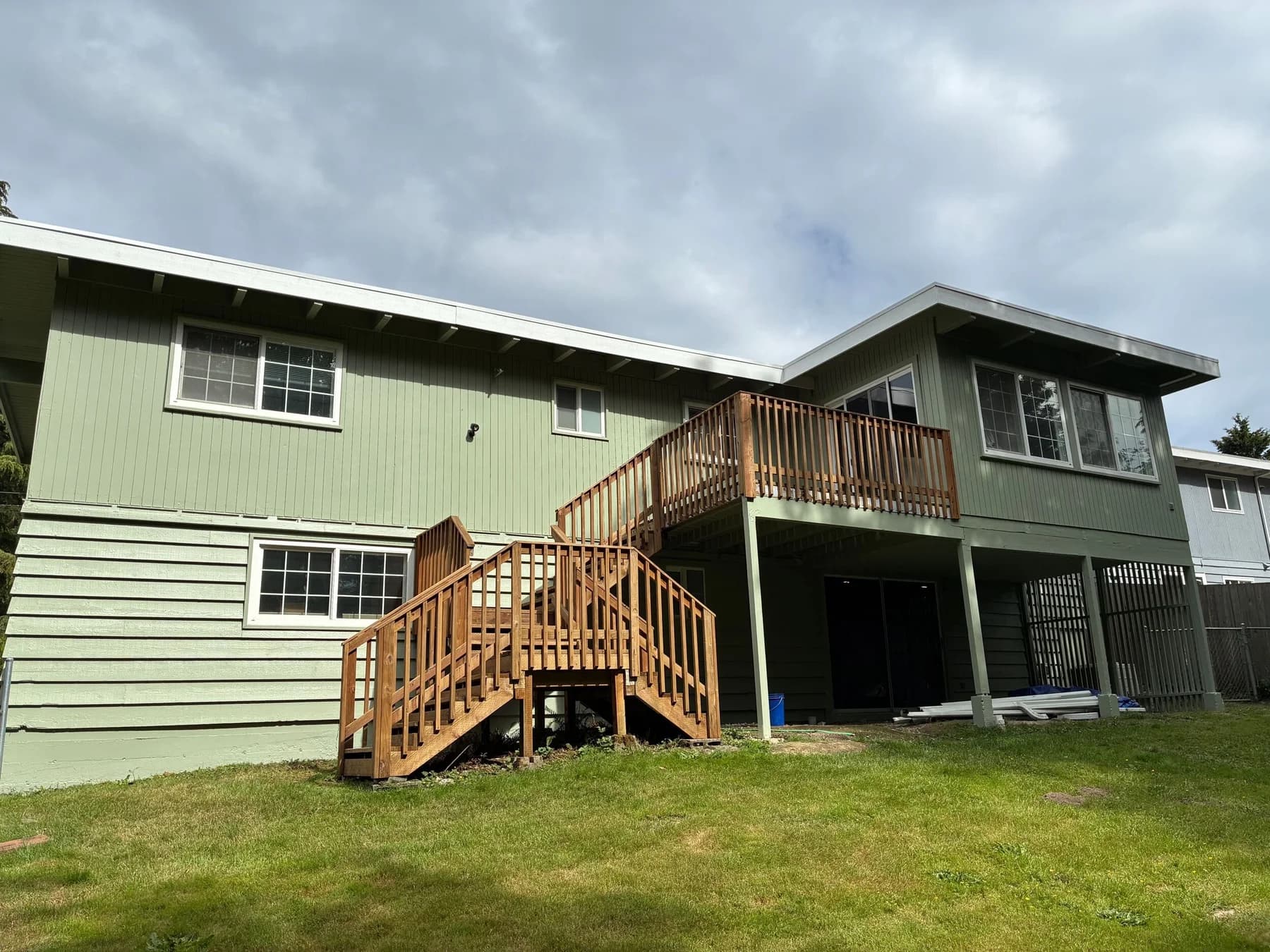 Exterior Painting — Rear elevation of a home with pale green siding, light trim, and a wood staircase