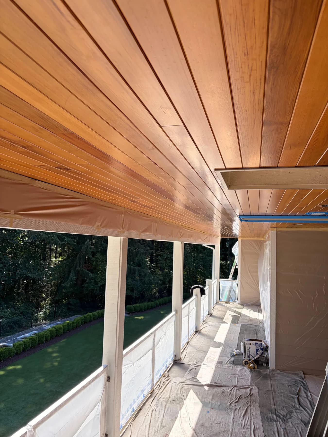 Soffit Staining — Stained wood soffit above a covered walkway with adjoining surfaces masked for finishing