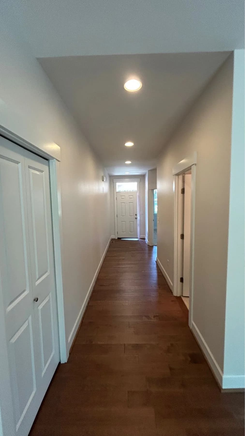 Interior Painting — Painted hallway with light walls, white doors and trim, recessed lighting, and wood flooring