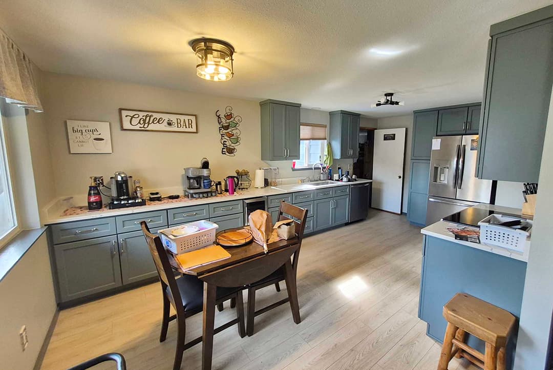 Kitchen with blue-gray cabinets, a small dining table, and stainless steel refrigerator
