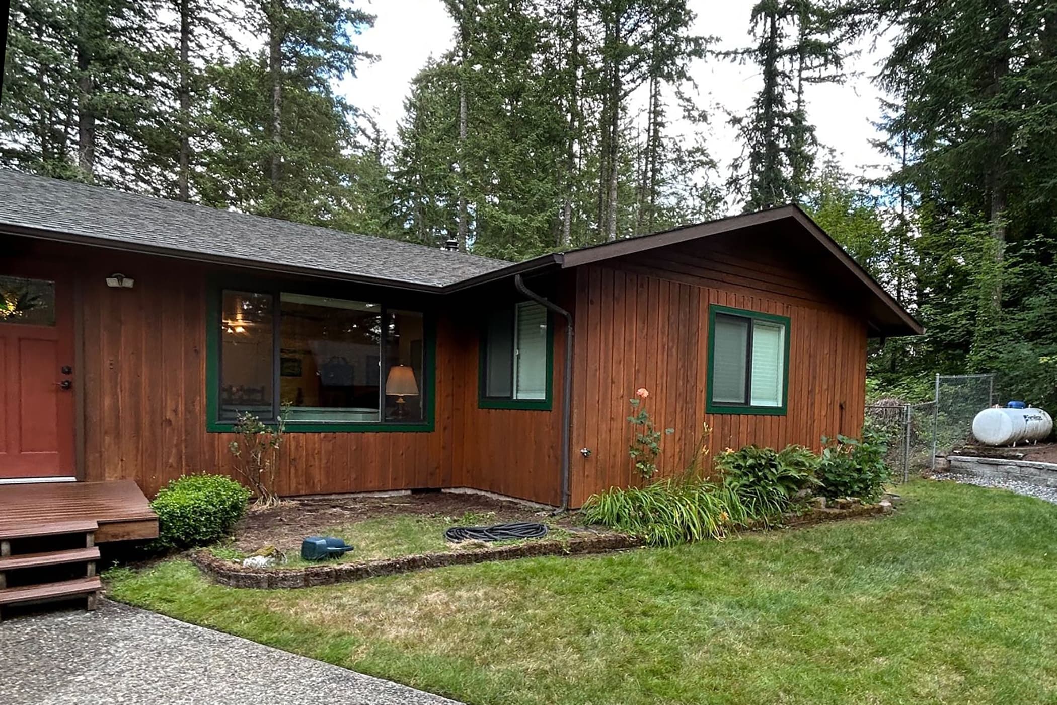Single-story house with warm brown vertical wood siding and green window trim