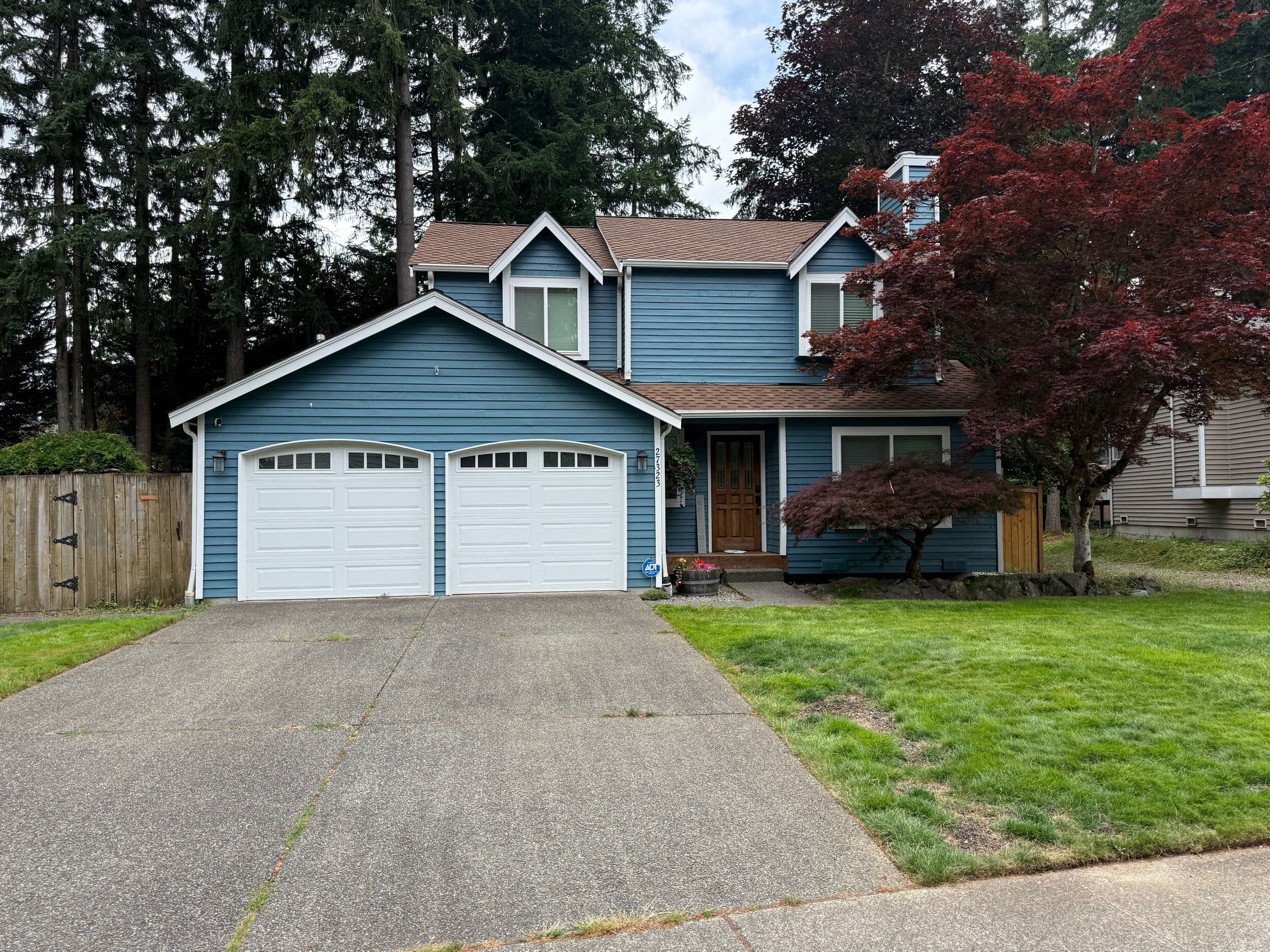 Blue two-story house with white trim, two garage doors, and mature trees