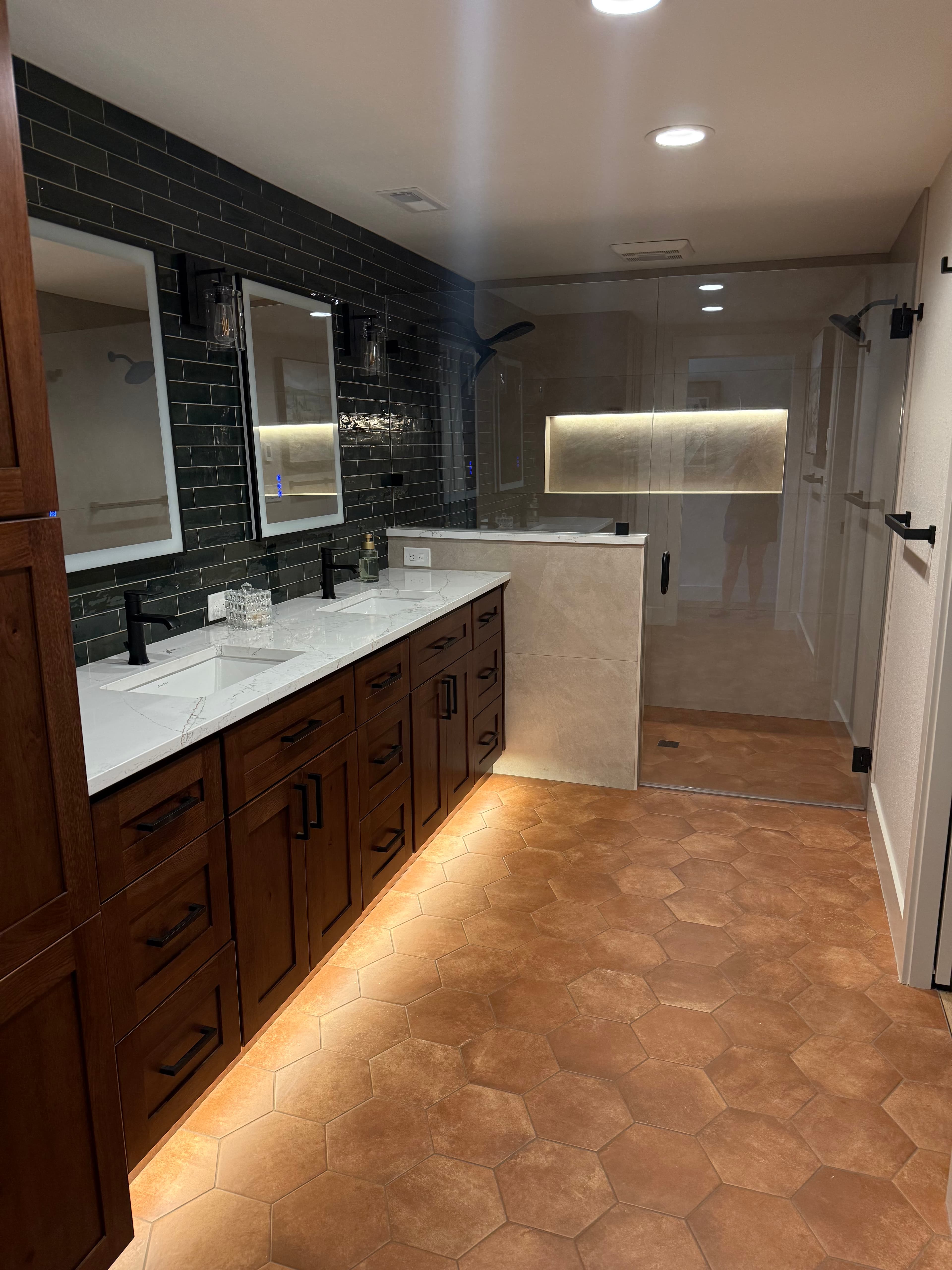 Bathroom with two vanity mirrors, wall sconces, recessed ceiling lights, and an illuminated shower niche